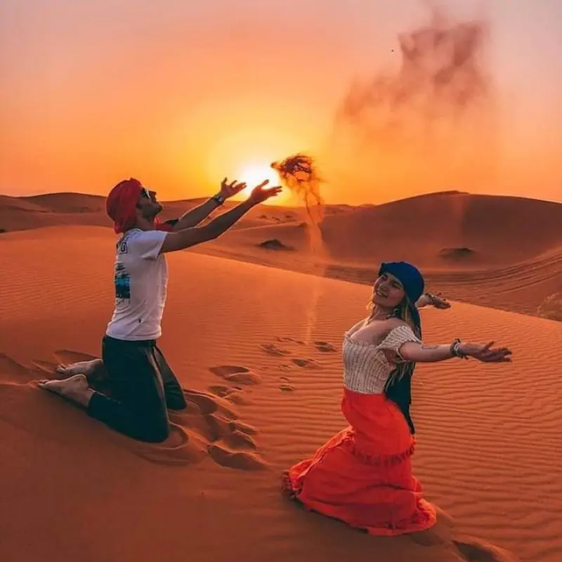 Couple throwing sand at sunset on the dunes of Erg Chebbi during a private 4-Day Marrakech to Merzouga Desert Tour